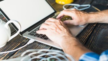 man-s-hand-typing-laptop-wooden-desk